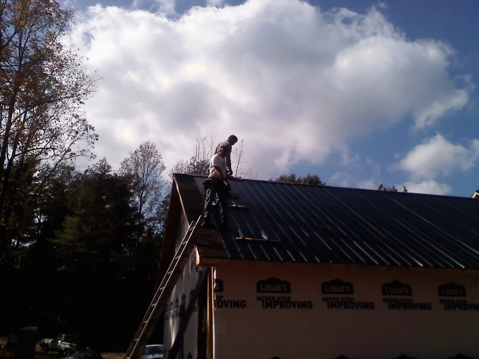 Roofer fastening dark metal panels high against a cloudy sky, from a Roof Inspection job in Marine On Saint Croix