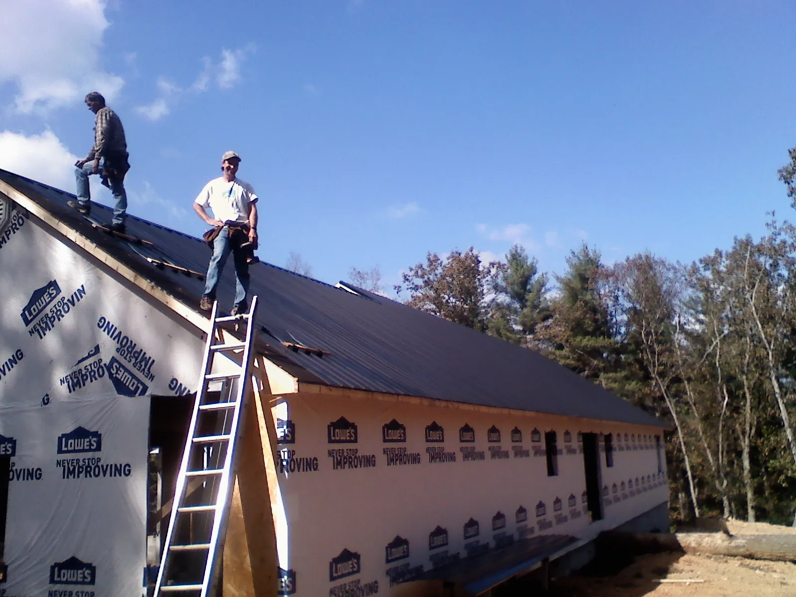 Two roofers standing on a long dark metal roof over a wrapped building in Marine On Saint Croix