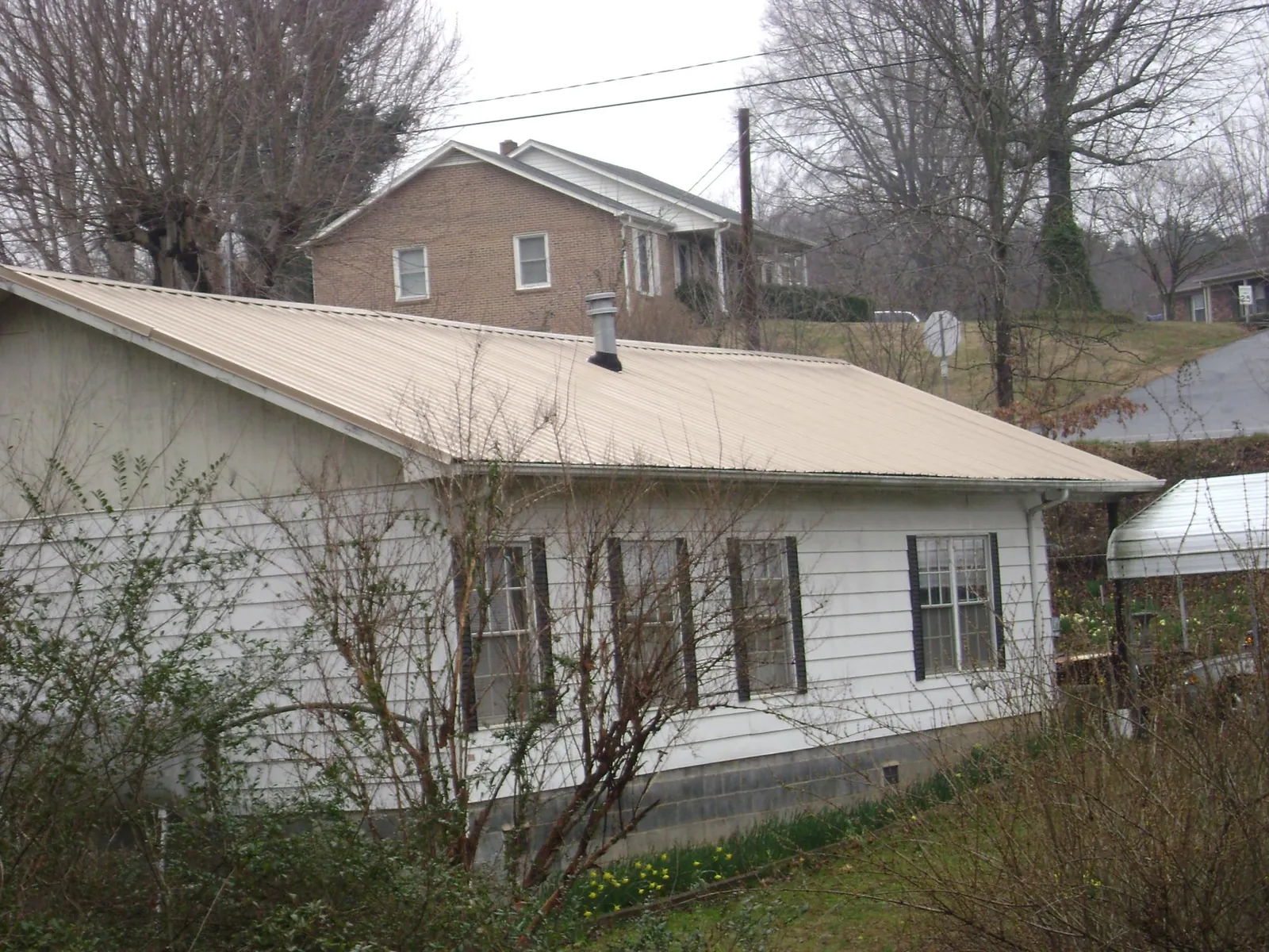 Tan metal roof on a white sided house set into a hillside — Commercial Roofing by Roofing Brothers in Marine On Saint Croix